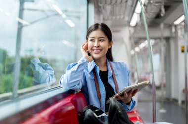 Genç ve güzel bir Asyalı kadın yolcu hayal kuruyor. Dışarıdaki manzaraya bakıyor. Bir gökyüzü treninde dijital tabletini kullanıyor..