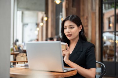 Siyah takım elbiseli zarif, kendine güvenen Asyalı bir iş kadını şehirdeki bir kafede bilgisayarını tamir ediyor ve uzaktan çalışıyor. Kablosuz teknoloji, şehir hayatı, iş adamları