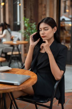 Belirsiz, düşünceli Asyalı bir iş kadını bir kafede oturmuş uzaktan çalışan bir kadınla telefonda konuşuyor. İnsanlar ve kablosuz teknoloji kavramları