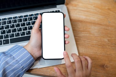 Ahşap bir masanın üzerinde elinde beyaz ekran maketi olan akıllı telefonu tutan bir kadının yakın plan görüntüsü. İnsanlar ve kablosuz teknoloji kavramları