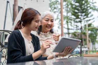 İlgili, pozitif, genç bir Asyalı torun büyükannesine bahçede dinlenirken dijital tablet kullanmayı öğretiyor. İnsanlar ve kablosuz teknoloji kavramları