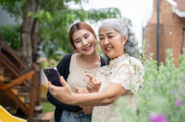 Sevimli bir Asyalı büyükanne torunuyla birlikte bahçede takılıp evde mutlu vakit geçirirken selfie çekiyor ya da video kaydediyor. Aile bağları, insanlar ve kablosuz teknoloji