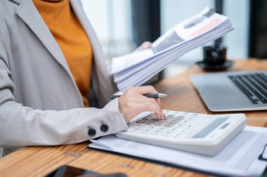 Ofisteki iş raporları üzerinde çalışırken hesap makinesi kullanan bir iş kadınının yakın plan görüntüsü..