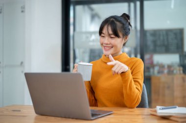 Güzel, neşeli Asyalı bir kadın bir kafeden uzaktan çalışıyor, ekibiyle çevrimiçi bir toplantı yapıyor, zoom yoluyla işi tartışıyor. insanlar ve teknoloji kavramları