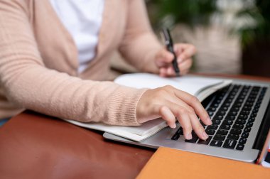 Laptop klavyesinde yazan hırkalı bir kadının kırpılmış görüntüsü ya da bilgisayarındaki bir çevrimiçi dersi incelerken Enter tuşuna basarak videoyu durdurma.