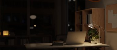 Geceleri modern karanlık bir ofis, masa başında dizüstü bilgisayar ve aksesuarlar, masa lambası ile aydınlatılmış. 3d görüntüleme, 3d illüstrasyon