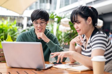 İki genç Asyalı üniversite öğrencisi dizüstü bilgisayar ekranına bakıyor ve şehirdeki bir kafede ortak bir proje üzerinde tartışıyorlar..