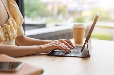 Dijital tablet kullanan, kablosuz klavyeye yazan, kapalı bir masada uzaktan çalışan bir kadının yakın plan görüntüsü. İnsanlar ve kablosuz teknoloji kavramları