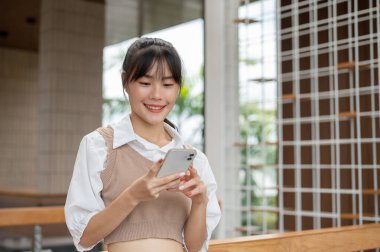 Güzel, mutlu, sıradan giysiler içinde genç bir Asyalı kadın binadayken birine mesaj atıyor ya da akıllı telefonunu kaydırıyor. İnsanlar ve kablosuz teknoloji kavramları