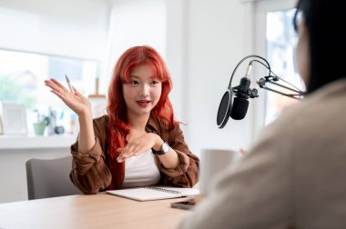 Kendine güvenen, arkadaş canlısı Asyalı bir kadın podcaster ya da kızıl kıvırcık saçlı içerik yaratıcısı stüdyosundaki bir misafirle röportaj yapıyor, sohbetin tadını çıkarıyor..