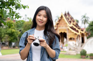Elinde kamera olan genç ve çekici bir Asyalı kadın yolcu kameraya gülümsüyor ve Chiang Mai 'deki Tayland Lanna tapınağını ziyaret ediyor..