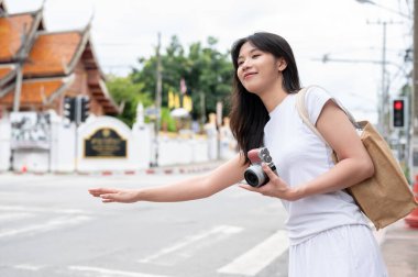 Olumlu, çekici genç Asyalı bir bayan turist Tayland 'da bir şehirde sokakta taksi yakalamak için elini sallıyor. seyahat, toplu taşıma, yaşam tarzları