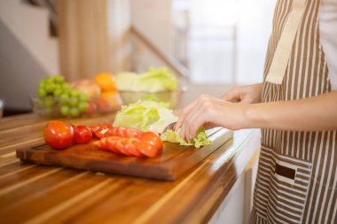 Mutfak masasında salatasına sebze hazırlarken ve evde yemek pişirirken marul doğrayan bir kadının yakın plan görüntüsü. diyet, sağlıklı yiyecekler, yaşam tarzı, eğlence