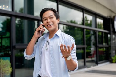 Yakışıklı bir Asyalı bina boyunca yürürken telefonda konuşuyor. kablosuz teknoloji ve yaşam tarzı kavramları
