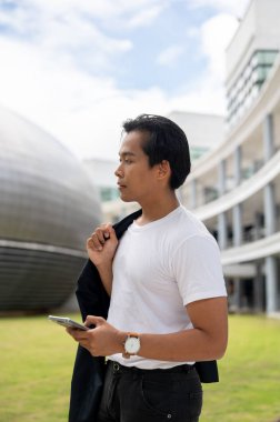 Takımını tutan yakışıklı bir Asyalı adamın portresi. Elinde akıllı bir telefonla dışarıda duruyor. Arka planda modern binalar var..