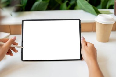 Dijital tabletini kullanan bir kadının kahve dükkanından uzaktan çekilmiş yakın plan görüntüsü. Tablet reklam için beyaz ekran modelini gösterir.