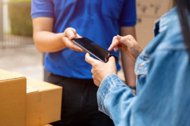 Bir bayan müşterinin yakın plan görüntüsü, paketlerini teslimatçıdan almadan önce akıllı telefondan imzalıyor, evinin önünde duruyor. Nakliye, taşıma, nakliye, ticaret.