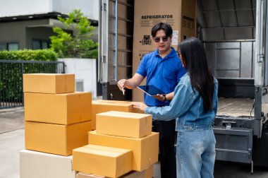 Mavi üniformalı Asyalı bir teslimatçı kamyonetinin arkasındaki kadın müşteriyle paketleri onaylıyor. Taşıma hizmeti, nakliye hizmeti, kargo lojistiği, nakliye