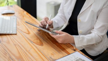 Ofisteki masasında dijital tabletini kullanan resmi takım elbiseli bir iş kadınının yakın plan resmi. Not alıyor. İş insanları ve kablosuz teknoloji kavramları