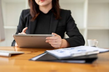 Ofisteki bir masada dijital tabletine konsantre olmuş siyah takım elbiseli bir iş kadınının kırpılmış görüntüsü. İş insanları ve kablosuz teknoloji kavramları