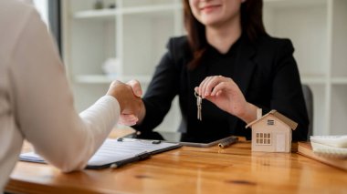 Kadın bir emlakçının iş yerinde bir müşteriyle buluşup sözleşme imzalarken ve el sıkışırken çekilmiş yakın plan görüntüsü. Ev kiralamak, mülk almak, iş görüşmesi.