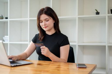 Evde bir masada dizüstü bilgisayarını kullanırken kredi kartına bakan güzel bir kadın. çevrimiçi ödeme, çevrimiçi alışveriş, mali yatırım