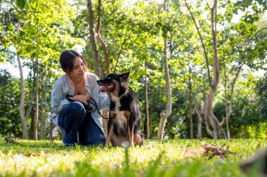 Asyalı bir kadın güneşli bir günde köpeğini parkta eğitiyor. Çimlerin üzerinde evcil hayvanıyla otururken dışarıda eğleniyor. Bağlanma, aşk, eğlence zamanı, insan ve hayvanlar