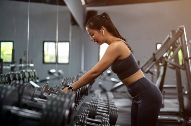 Spor giyim giymiş güzel, sportif Asyalı bir kadının spor salonundaki spor yaparken askıya bir dambıl koyuşunun yan görüntüsü. eğitim, egzersiz, fitness, sağlıklı yaşam tarzı