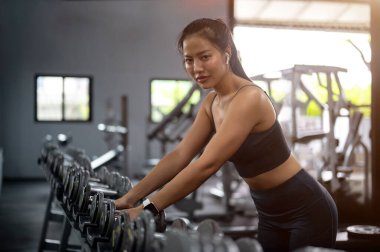 Spor giyim giymiş güzel, sportif Asyalı bir kadının spor salonundaki spor yaparken askıya bir dambıl koyuşunun yan görüntüsü. eğitim, egzersiz, fitness, sağlıklı yaşam tarzı