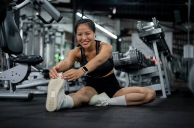 Spor kıyafetleri içinde çekici bir Asyalı kadın spor salonunda oturuyor, bacaklarını esnetiyor, antrenmandan önce ısınıyor ya da sonra serinliyor. insanlar ve spor kavramları