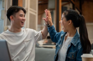 İki neşeli ve heyecanlı Asyalı genç arkadaş birlikte iyi haberi kutluyorlar, birbirlerine aşırı neşeli ifadelerle beşlik çakıyorlar. Takım çalışması, arkadaşlık, meslektaş, en iyi arkadaş