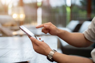 Bir kafede otururken akıllı telefonunu kullanan bir adamın yakın plan görüntüsü. Sohbete cevap vermek, telefonunu kaydırmak, mesajları okumak, mobil uygulama kullanmak, internetten alışveriş yapmak.