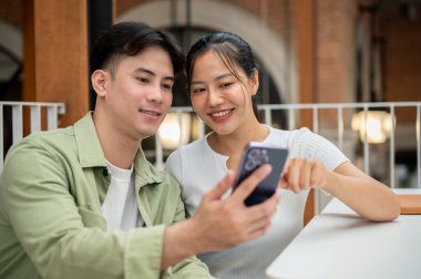 Mutlu, sevimli, genç bir Asyalı çift, erkek arkadaş ve kız arkadaş, sohbet ediyorlar ve bir kafede akıllı telefondan video izliyorlar. İnsanlar, yaşam tarzı, kablosuz teknoloji