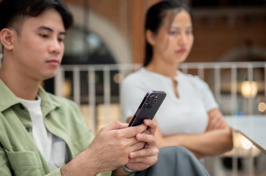 Ciddi bir Asyalı genç adam telefonunu kaydırıyor. Huysuz kız arkadaşını bir kafede yan yana otururken görmezden geliyor. İlişki sorunları yaşıyor..