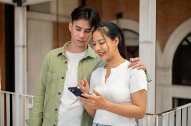 Güzel, mutlu bir Asyalı çift evde dikilirken akıllı telefondan video falan izliyor. Mutlu bir ilişki, çift hedefi, sevgili ve sevgili