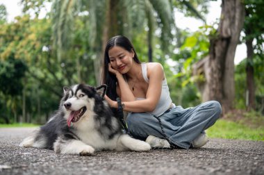 Tasmalı güzel bir Sibirya köpeği ve Asyalı bayan sahibi yeşil bir parkta birlikte oturuyorlar ve dışarıda eğleniyorlar. Hayvan, hayvan, en iyi arkadaş.