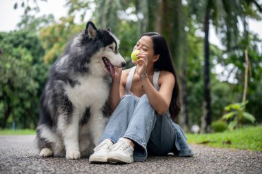 Güzel bir Asyalı bayan köpek sahibi yeşil bir parkta oturuyor, köpeğiyle oynuyor ve ona itaat etmesini ve top alması için el sıkışmasını öğretiyor..