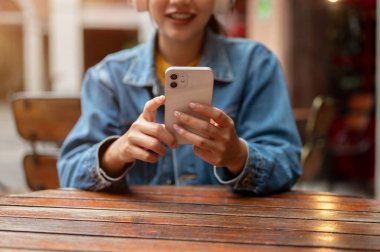 Açık bir masada otururken akıllı telefon kullanan kot ceketli Asyalı bir kadının kırpılmış görüntüsü. cep telefonu uygulaması kullanarak mesajları okumak, sohbet etmek, kaydırmak.