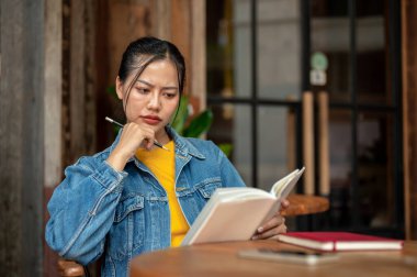 Kot ceketli ciddi bir Asyalı kadın kafeteryada otururken kitap okumaya odaklanıyor. insanlar ve yaşam tarzı kavramları