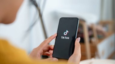 Chiang Mai, Tayland - Sep 19 2024: Evde bir kanepede otururken iPhone 'undaki TikTok uygulamasını kullanan bir kadının yakın çekimi. Sosyal medya platformu, mobil uygulama, kablosuz teknoloji