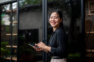 Kendine güvenen, çekici Asyalı bir iş kadını elinde akıllı bir telefonla ofis koridorunda yürüyor ve kameraya gülümsüyor. İnsanlar ve kablosuz teknoloji kavramları