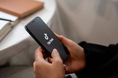 Chiang Mai, Tayland - Ekim 03 2024: Ekranda TikTok logosu olan iPhone tutan bir kadının yakın çekimi. Evde otururken akıllı telefonuyla TikTok kullanan bir kadın..