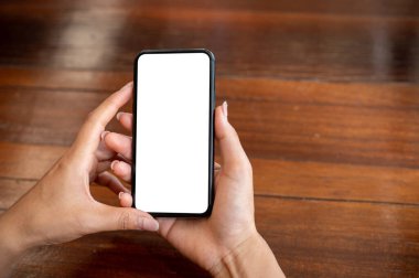 İçerideki ahşap bir masada oturan ve akıllı telefonunu kullanan beyaz ekran görüntülü akıllı telefonu olan bir kadının yakın çekimi. İnsanlar ve kablosuz teknoloji kavramları