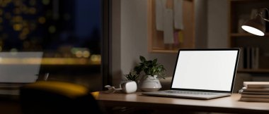 Beyaz ekran maketi, kulaklık, kitap ve dekoratif bitkilerle dolu bir dizüstü bilgisayar. Gece bir masa lambasıyla aydınlatılıyor. Geceleri ofis, 3D resim, 3D resim