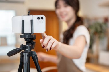 Kamerayı ayarlamak için akıllı telefon ekranına dokunan bir kadının yakın plan fotoğrafı mutfakta yemek pişirirken kamerayı ayarlamak için, akıllı telefon tripoda yerleştirilmiş. içerik oluşturucu, yiyecek blogcusu