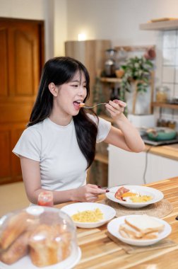 Çekici, çekici, genç Asyalı bir kadın mutfak adasında ya da yemek masasında kahvaltının tadını çıkarıyor. Yaşam tarzı, ev hayatı, yemek, insanlar