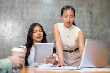 İki çekici Asyalı iş kadını, ekibiyle yaptıkları toplantıda dizüstü bilgisayardaki bir projeyi incelemeye odaklanmış durumdalar. Girişim grubu, iş toplantısı, danışma, beyin fırtınası, takım çalışması