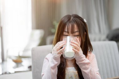 Genç, tapılası bir Asyalı çocuk kahvaltı sırasında yemek masasında bir bardak sütün tadını çıkarıyor..