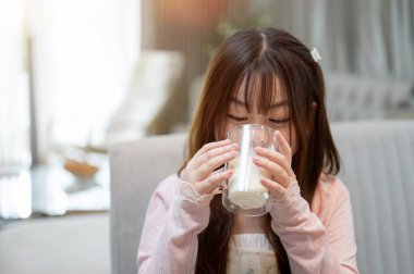 Genç, tapılası bir Asyalı çocuk kahvaltı sırasında yemek masasında bir bardak sütün tadını çıkarıyor..