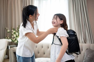 Güzel, şefkatli bir Asyalı anne, küçük kızıyla sohbet ederken sabahleyin oturma odasında okula hazırlanmasına yardım ediyor. Mutlu aile anları, aile bağları